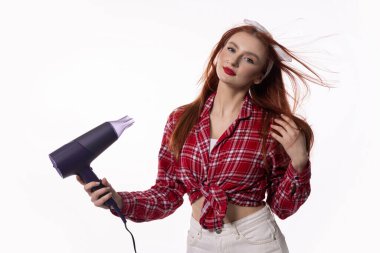 Kendine güvenen ve şık bir model şık bir kıyafet giyerken saç kurutma makinesi kullanarak lüks saç bakımı sergiliyor.