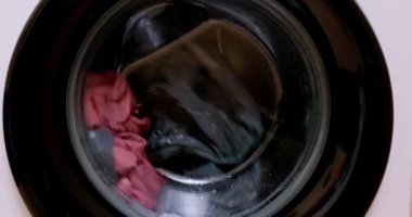 Bu, çamaşır makinesinin variline yerleştirilmiş renkli giysileri gösteren yakın plan bir görüntü.