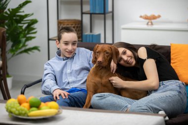 Neşeli ve mutlu bir aile, sevgili köpekleriyle aydınlık ve sıcak bir oturma odasında vakit geçirmekten zevk alır.