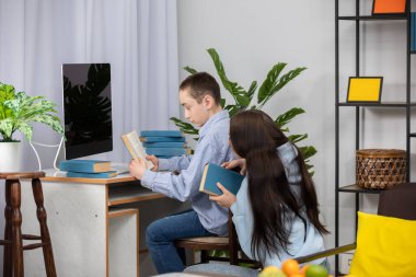 İki çocuk, çeşitli kitaplar ve teknolojilerle çevrili olarak evde birlikte okuyorlar ve okuyorlar.