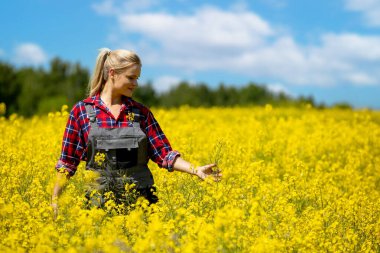 Tulum giymiş dişi bir çiftçi güneşli bir gökyüzünün altındaki geniş sarı çiçek tarlasını mutlulukla keşfeder.