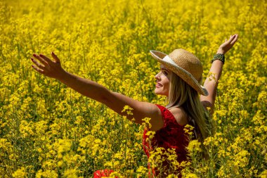 Neşeli bir kadın kendini doğaya daldırıyor, sıcak güneşin altında canlı sarı bir çiçek tarlasının tadını çıkarıyor.