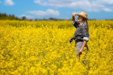 Bir kadın neşeli bir şekilde, parlak mavi gökyüzünün altında, doğayı kucaklayan, canlı sarı çiçekleri keşfeder.