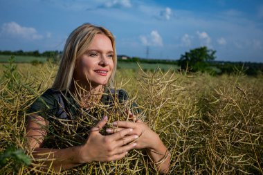 Güzel ve dingin bir portre. Açık mavi gökyüzünün altındaki altın tarlalarda huzur içinde duran bir kadın.