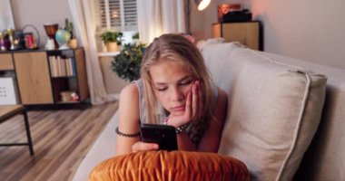 Bir kız, modaya uygun, çağdaş bir yaşam ortamında akıllı telefonunun tadını çıkarırken rahat bir kanepede dinlenir.