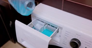Çamaşır makinesinin yakın plan görüntüsü. Sıvı deterjan kutusu dikkatlice dolduruluyor.