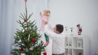 Sevgi dolu bir babanın Noel ağacını süslemek için kızını kaldırdığı neşeli bir sahne.