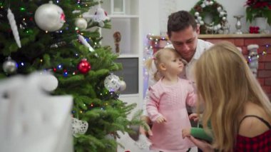 Güzel dekore edilmiş bir Noel ağacı tarafından paylaşılan neşeli bir aile anı, şenlikli süslerle süslenmiş.