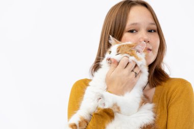 Parlak bir stüdyoda, genç bir kadın tüylü turuncu ve beyaz kedisini neşeyle kucağına alır, sıcaklık ve mutluluk saçar.