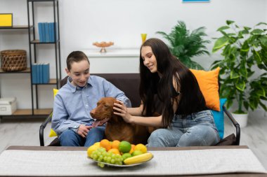 Mutlu bir çocuk, şefkatli bir kadın ve tapılası bir köpekle evde taze meyvenin tadını çıkaran neşeli bir aile anı.