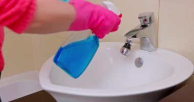 Temizliği sağlama almak için çağdaş bir banyo lavabosunu sprey şişesi ve bezle özenle temizleyen biri.