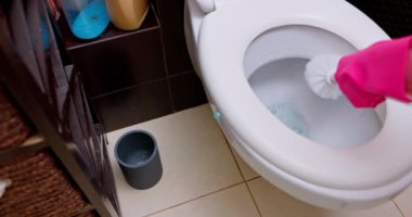 Pürüzsüz, modern bir banyo ortamında dezenfektanla tuvaleti özenle temizleyen birinin yakın çekim görüntüsü.