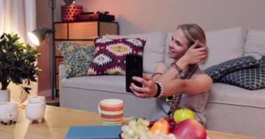 Neşeli genç bir kız sıcak bir oturma odasında selfie çekmek için neşeli bir poz veriyor.