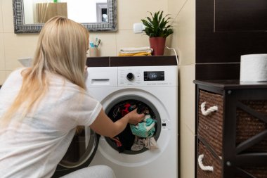Bir kadın renkli giysilerini şık bir çamaşırhanede bulunan modern bir çamaşır makinesine yüklüyor.