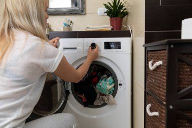 Bir kadın, modern bir çamaşır odasında bulunan çamaşır makinesinin çeşitli ayarlarını ustalıkla ayarlar.