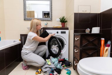 Bir kadın şık ve modern bir banyoda çamaşırlarını yıkamakla meşgul. Dekorasyonla birlikte bir de çamaşır makinesi var.