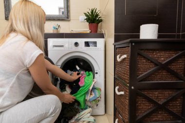 Şık ve modern bir iç dekorda bir kadın, renkli giysileri dikkatlice çamaşır makinesine yerleştirir.