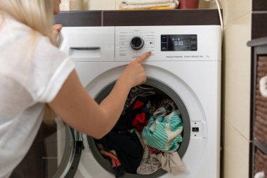 Renkli giysilerle dolu bir çamaşır makinesini ustalıkla çalıştıran bir kadın modern çamaşır teknolojisi sergiliyor.