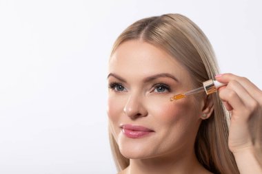 Bir kadın lüks bir yüz serumu uygulamak için ustalıkla bir damlatıcıyı kullanıyor. Detaylı cilt bakımını gösteriyor.