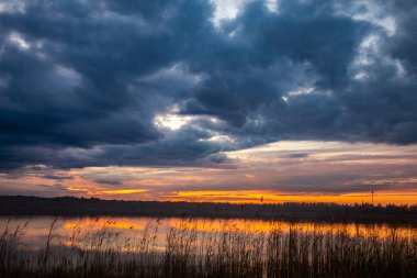 Gün batımında dingin bir göl, canlı renkler ve karamsar bulutlar, doğa severler ve fotoğrafçılar için mükemmel.