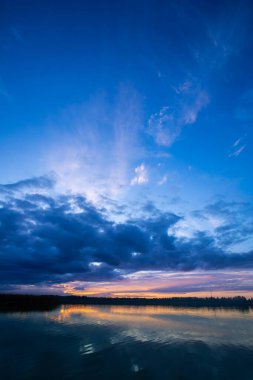 Nefes kesen bir günbatımı, sakin sulara canlı ve çarpıcı renkler ve yukarıda dramatik bir gökyüzü sergiliyor.