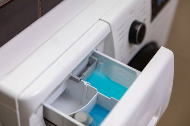 Çamaşır makinesinin yakın çekim görüntüsü. Parlak mavi sıvı deterjan dolu deterjan çekmecesi.