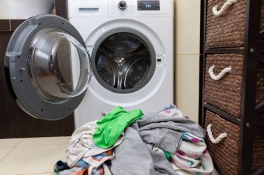 Şık, modern bir çamaşır makinesi. Çamaşırhaneye hazır rengarenk kıyafetlerin yanına yerleştirilmiş.