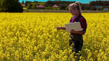 Bir kadın canlı sarı bir çiçek tarlasında dizüstü bilgisayar kullanarak doğayı teknolojiyle harmanlıyor..