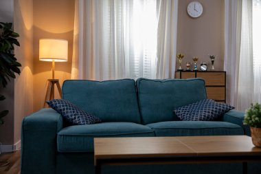 İçinde mavi bir kanepe, ahşap bir sehpa ve güzel yumuşak bir ışıklandırma olan büyüleyici bir oturma odası.