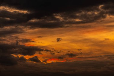 Koyu bulutlar ve parlak turuncu renklerin yer aldığı nefes kesici bir gün batımı manzarası gökyüzünü güzel aydınlatıyor.