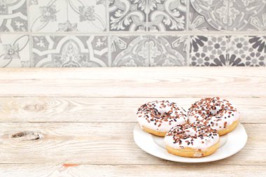 Renkli kremayla kaplanmış üç lezzetli çörek ve çikolata parçacıkları ahşap bir masanın üzerinde güzel bir şekilde duruyor.