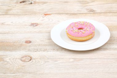 Beyaz bir tabakta çeşitli renklerde serpiştirilmiş nefis pembe şekerli donut.