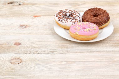 Renkli bir pembe, çikolata ve beyaz şekerli çörekler kırsal ahşap bir masa üzerinde ustalıkla düzenlenmiş.