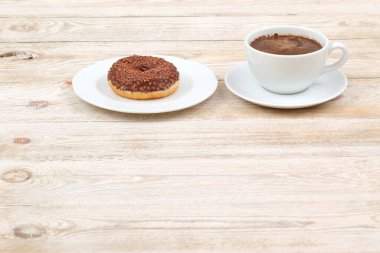 Nefis bir şekilde cezbedici bir çikolatalı çörek, ahşap bir masada, dumanı tüten bir fincan taze kahveyle çok güzel eşleştirilmiş.