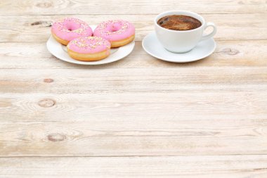 Lezzetli pembe çöreklerle ve kırsal ahşap bir masada bir fincan kahveyle sıcacık ve keyifli bir anın tadını çıkar.