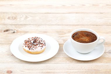 Çikolata parçacıklarıyla kaplı lezzetli bir donut, ahşap bir masada, dumanı tüten bir fincan kahvenin yanında duruyor.