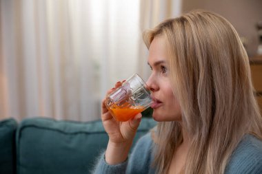 Neşeli bir kadın evinde rahatlar, renkli bir içki yudumlarken sıcak, davetkar bir atmosfer yaratır.