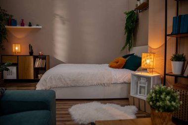 Sıcak ışıklandırma, bereketli bitkiler ve çağdaş bir estetik tasarım içeren şık ve davetkar bir yatak odası.