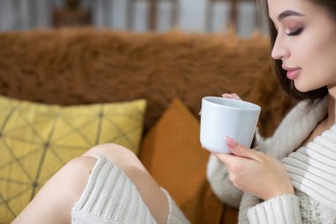 Yumuşak dokular ve rahatlatıcı renklerle dolu, rahat ve şık bir ortamda sıcak bir içkinin tadını çıkaran bir kadın.