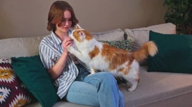 Bir kadın neşeli bir şekilde kedisini rahat bir koltukta kucaklıyor, canlı yastıklarla çevrili, sıcak, mutlu bir ev yaratıyor.