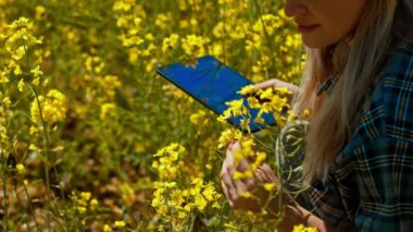 Bir kadın, doğada bol miktarda canlı sarı çiçeklerle çevriliyken bir tabletle neşe içinde etkileşime girer.