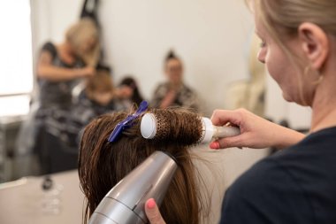 Yetenekli bir stilist şık bir kuaförde saç kurutma makinesi ve bigudiler kullanır.