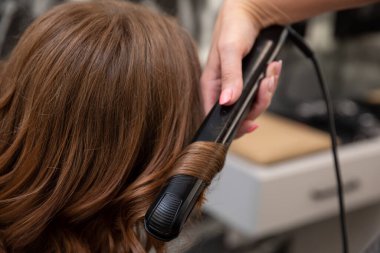 Çok yetenekli bir stilist, bir saç düzleştiricisini müşterisinin saçında güzel ve çarpıcı kıvrımlar yapmak için ustalıkla kullanır.