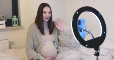 Hamile bir kadın yatak odasında halkalı ışıkla aydınlatılan içeriği kaydederken sessiz bir anın tadını çıkarıyor..