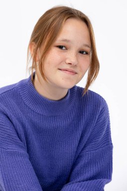 Genç bir kadın rahat mavi bir süveter giyerken hafifçe gülümsüyor, samimiyet ve yakınlık hissi yayıyor.