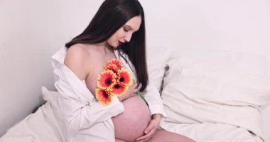 Akan beyaz gömlekli hamile bir kadının huzurlu portresi. Çiçeklerle güzelliğini kucaklıyor.