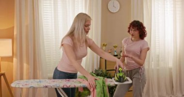 İki iyi arkadaş, sıcak ve misafirperver doğal ışıkla dolu parlak, rahat bir odada giysilerini ütülüyorlar.