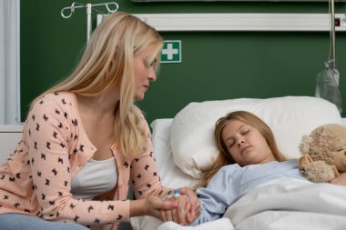 Şefkatli bir anne kızını bir hastane yatağında teselli eder. Güçlü sevgi ve destek bağlarını gösterir.