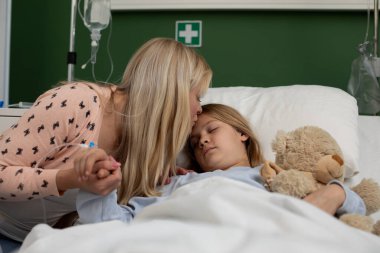 Bir anne hasta çocuğunu bir hastane yatağında rahat ettirir. Zor zamanlarda derin sevgi ve ilgi gösterir.