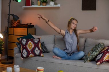 Neşeli genç bir kadın, rahat bir oturma odasında renkli yastıklarla çevrili kanepesine uzanır..